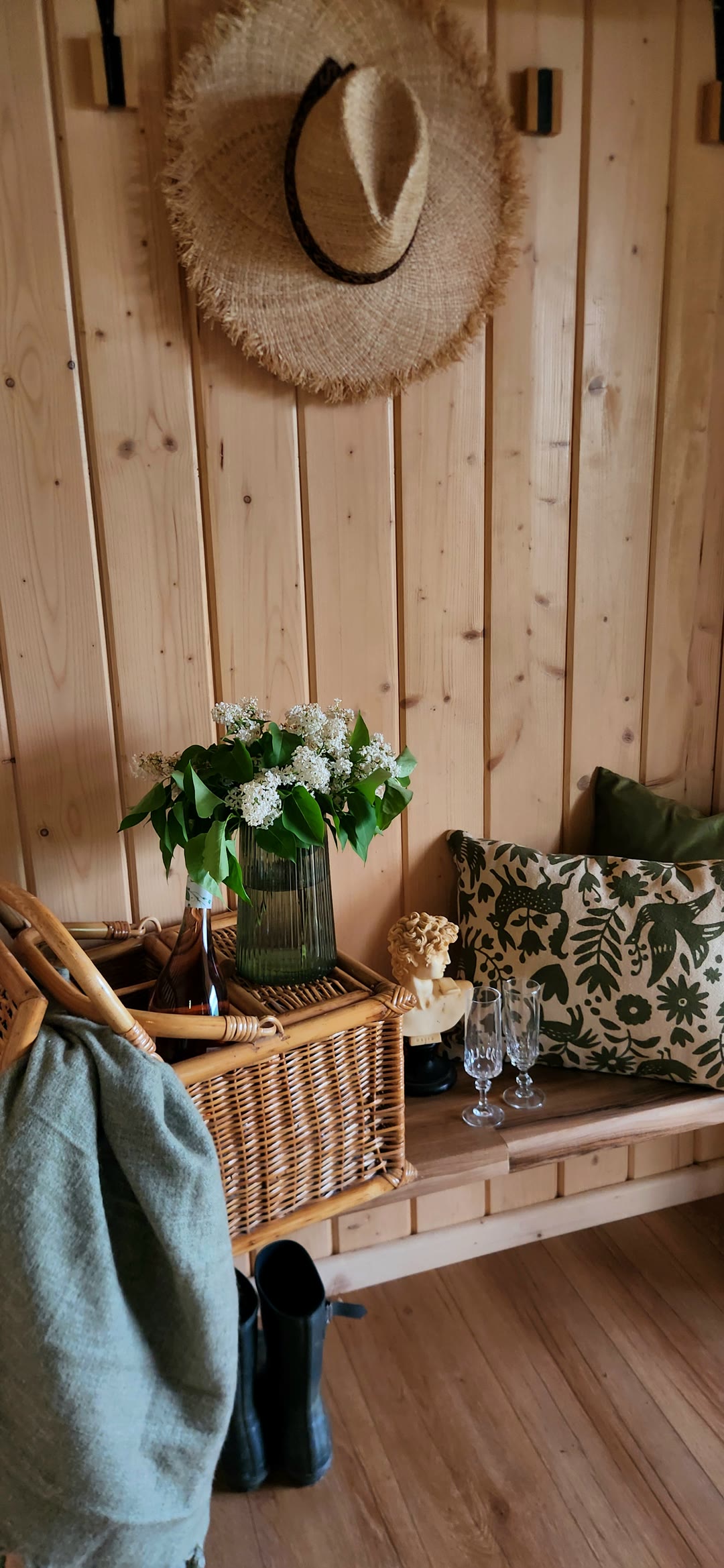 A straw hat, lilac in a green vase and embroidered cushions on the bench