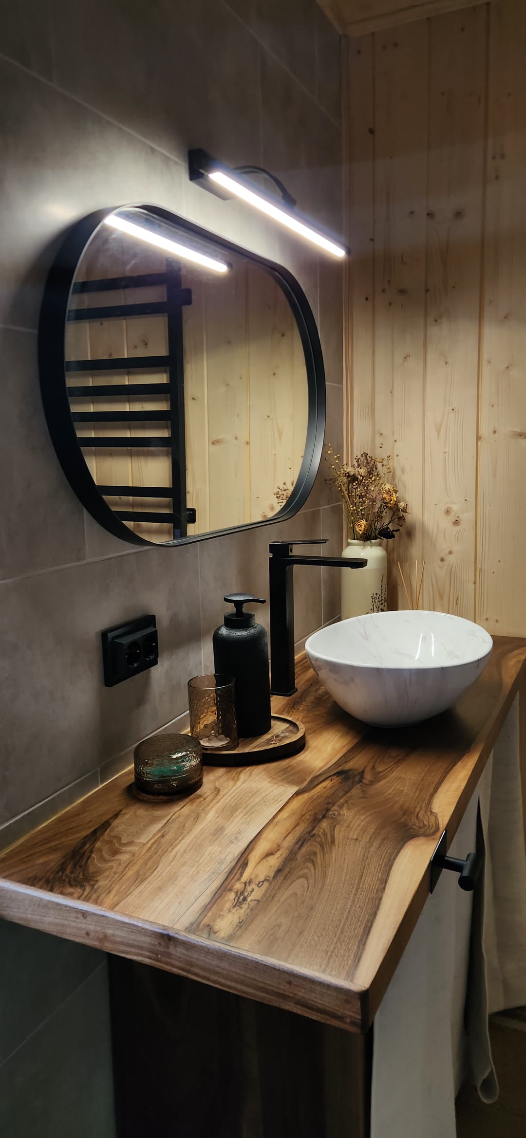 A basin on a walnut counter under a round mirror
