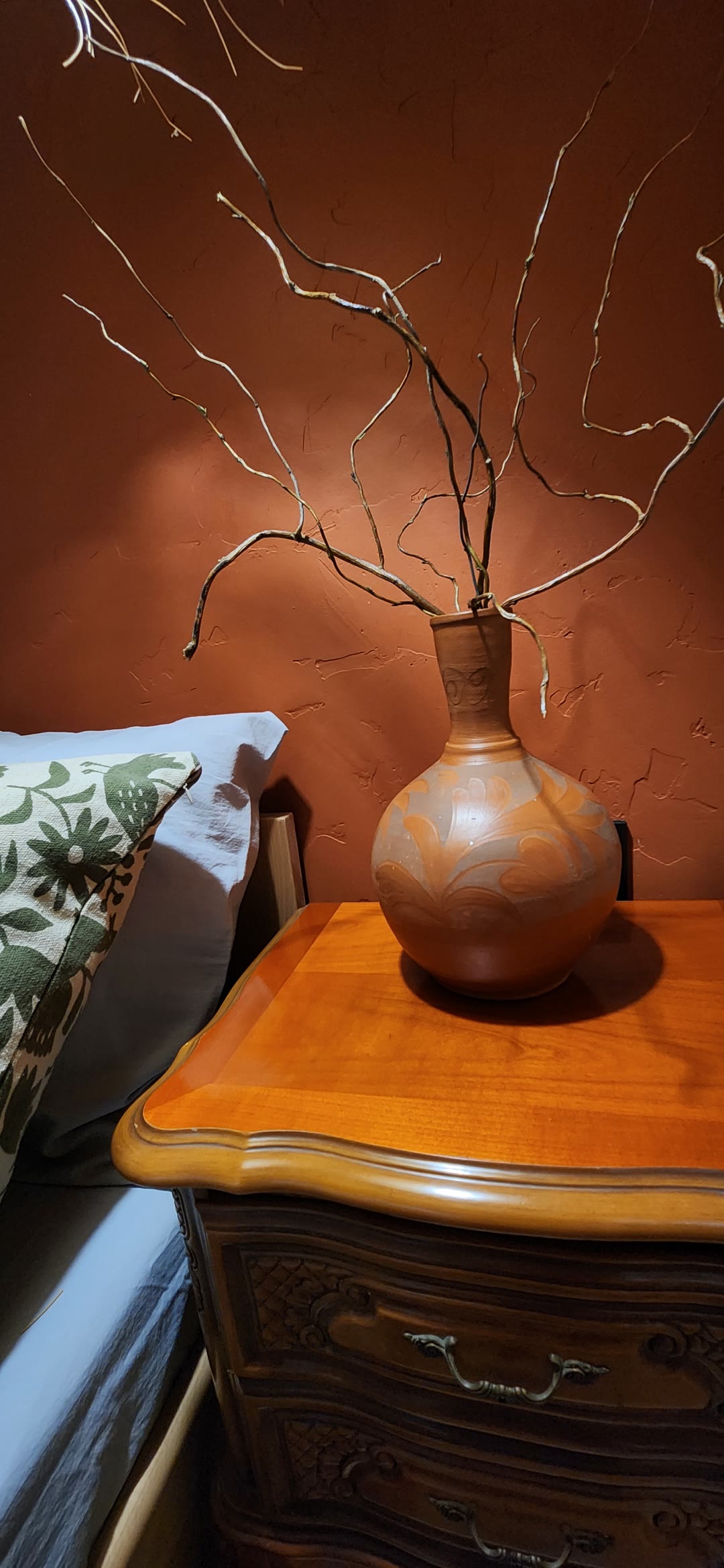 A clay vase with branches on a carved bedside table