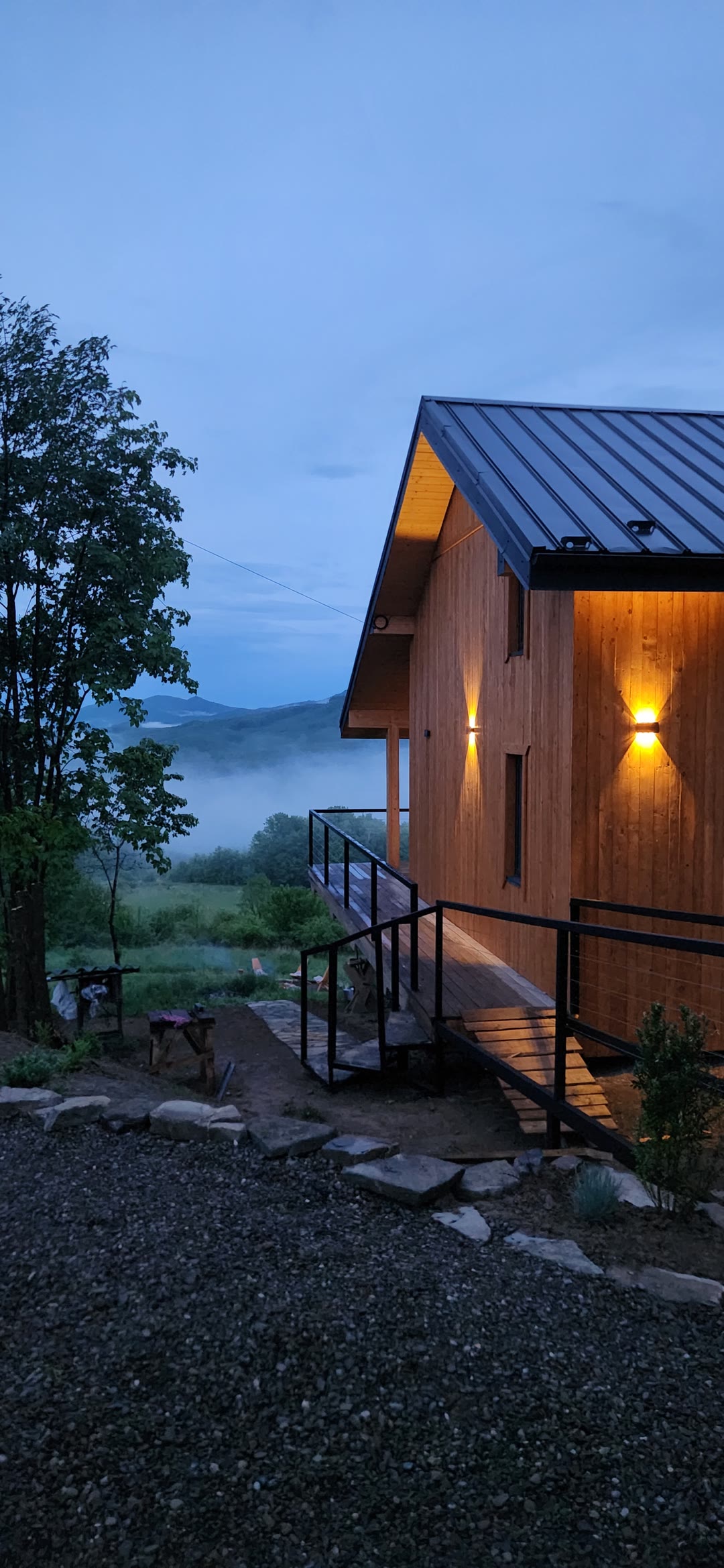 Yutori at dusk: a timber house with warm wall lights, fog in the valley below