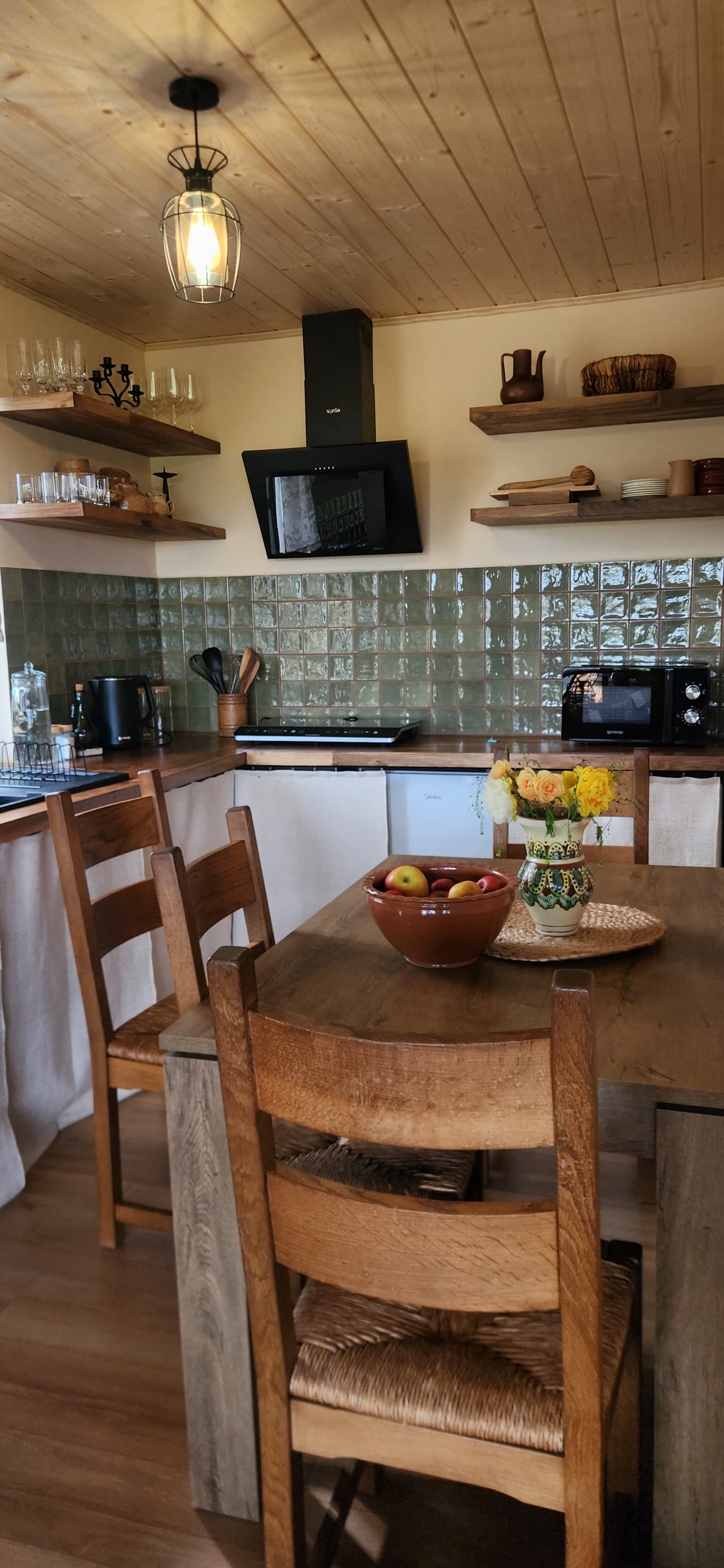 The kitchen with green tiles, open shelves and a dining table