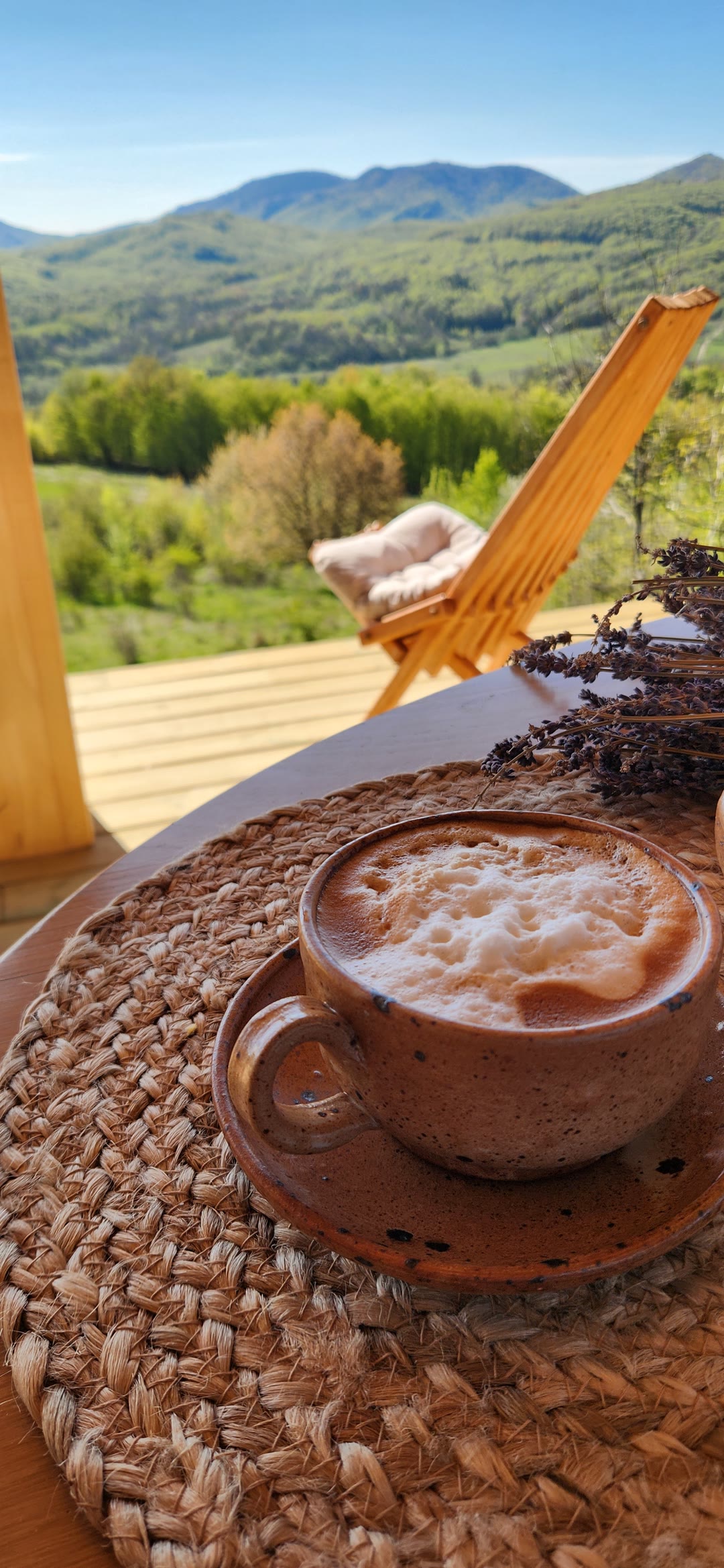 A cappuccino on a woven mat, lavender and a chair on the terrace