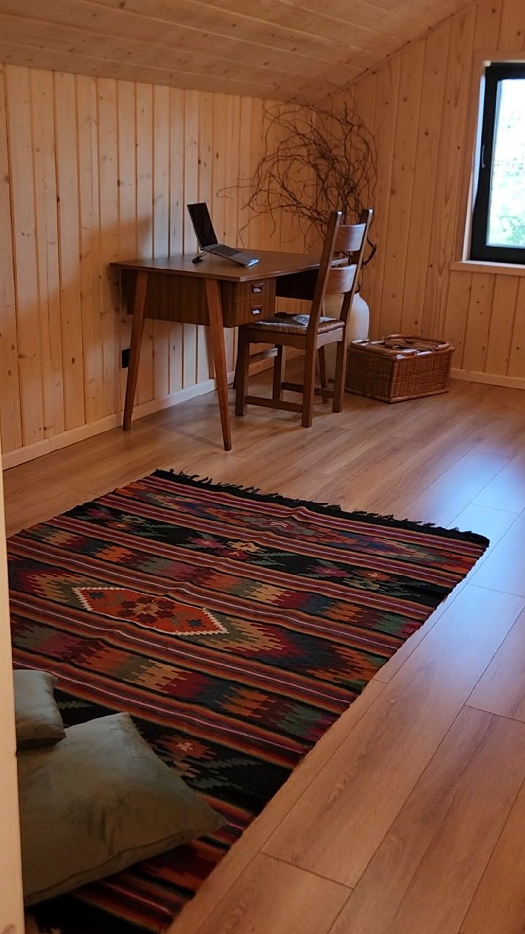 A desk with a laptop, a wicker basket and a rug